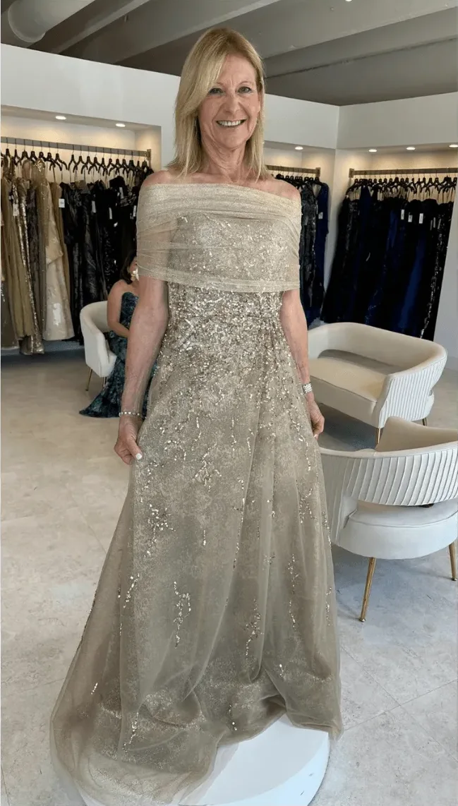 A client in a champagne beaded gown on the fitting platform, with the rails behind her